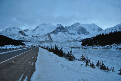 Snow covered road by snowcapped mountains against sky