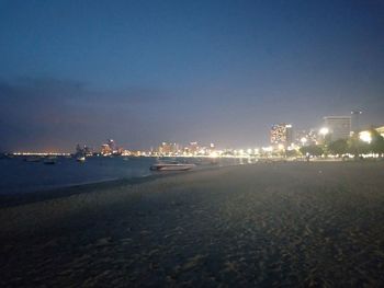 Illuminated buildings by sea against sky at night