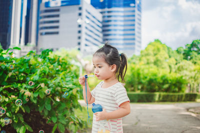 Girl blowing bubbles by plants at park