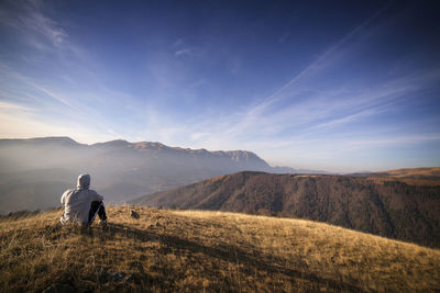 Rear view of man standing on mountain against sky during sunset