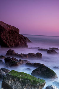 Scenic view of rocks on beach against sky during sunset