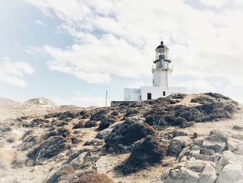 Lighthouse on cliff by sea against sky