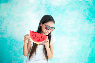 Happy teenage girl having watermelon while standing by turquoise wall