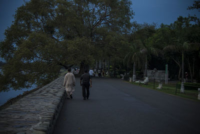 Rear view of people walking on road against trees