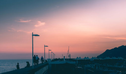 Silhouette street by sea against sky during sunset