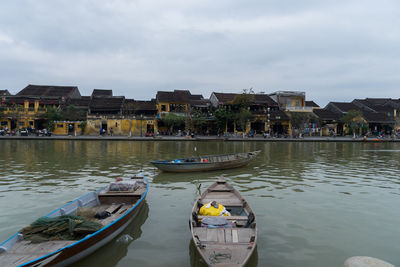 Boats moored in lake against sky in city