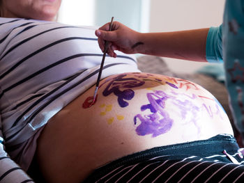 Midsection of girl painting pregnant mother belly at home