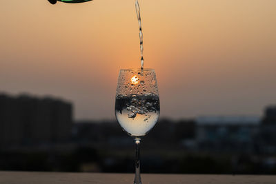 Clear liquid being poured into a wine glass at sunset