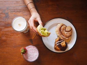 Cropped image of woman holding donut with breakfast on table