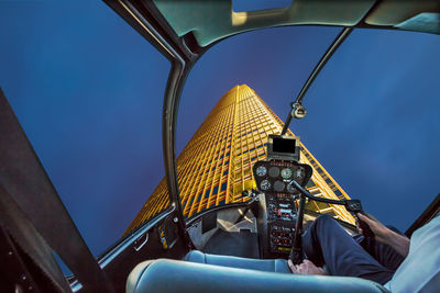 Midsection of pilot flying helicopter by skyscraper against sky