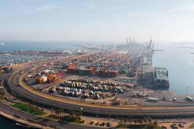 Drone view of valencia port with cargo containers and cars near ship located on seashore under blue sky in sunlight