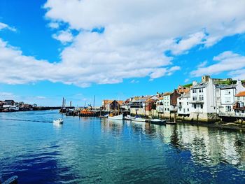 Sailboats moored on sea by buildings against sky