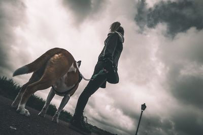 Low angle view of woman with dog standing on street against cloudy sky