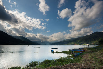 Boats in lake against cloudy sky