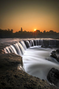 Scenic view of waterfall against sky during sunset