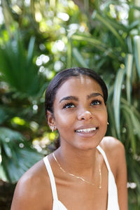 Smiling young woman looking away against plants