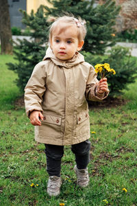 Little toddler baby girl in trench coat picking yellow dandelions in spring garden. cute baby girl