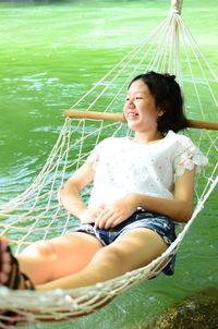 Smiling teenage girl lying on hammock by river