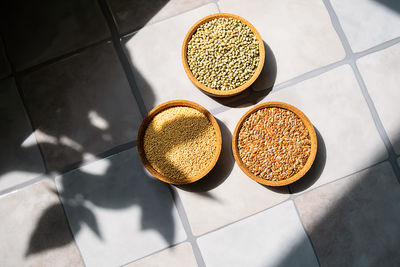 Three bowls with amaranth, flax and hemp seeds on a tile surface with sunlight. 