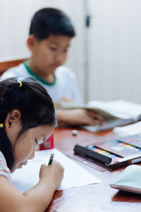 Siblings studying while sitting on table