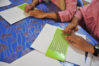 Cropped hand of people studying braille on table