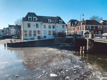 Buildings by river against blue sky