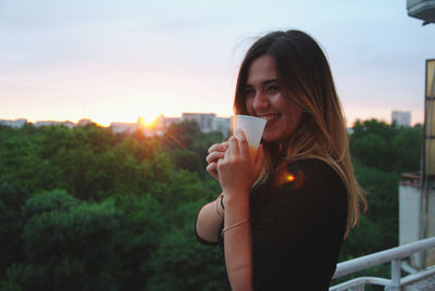 Beautiful young woman drinking drink at sunset