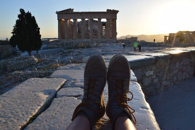 Low section of person legs by parthenon against clear sky during sunset