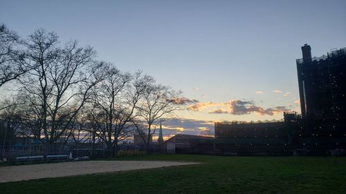 Park by buildings against sky during sunset