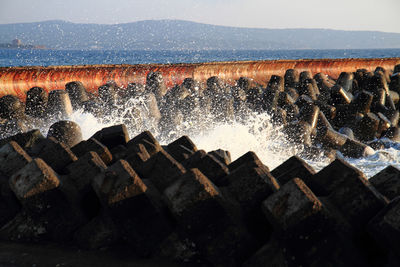 Water splashing on rocks by sea against sky