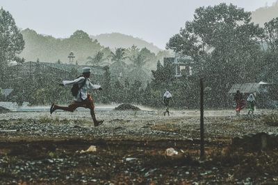 People playing on field by trees against sky