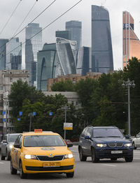 Cars on road by buildings against sky in city