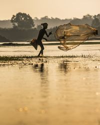 Side view of man catching fish on the river bank.