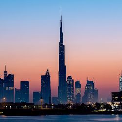 Illuminated burj khalifa amidst buildings in city against sky during sunset