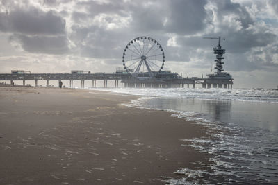 Ferris wheel at beach against cloudy sky