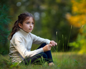 Cute girl looking away while sitting on grass at park