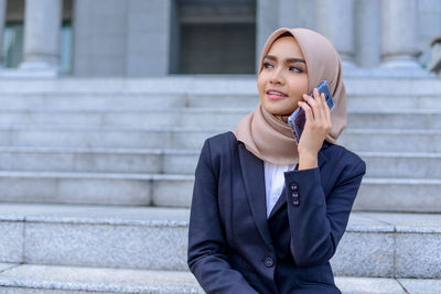 Happy young woman looking away while sitting on staircase