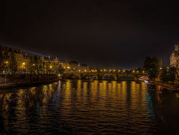 Illuminated bridge over river in city against sky at night