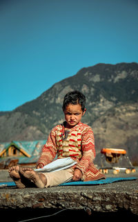 Girl child sitting with a notebook against clear sky
