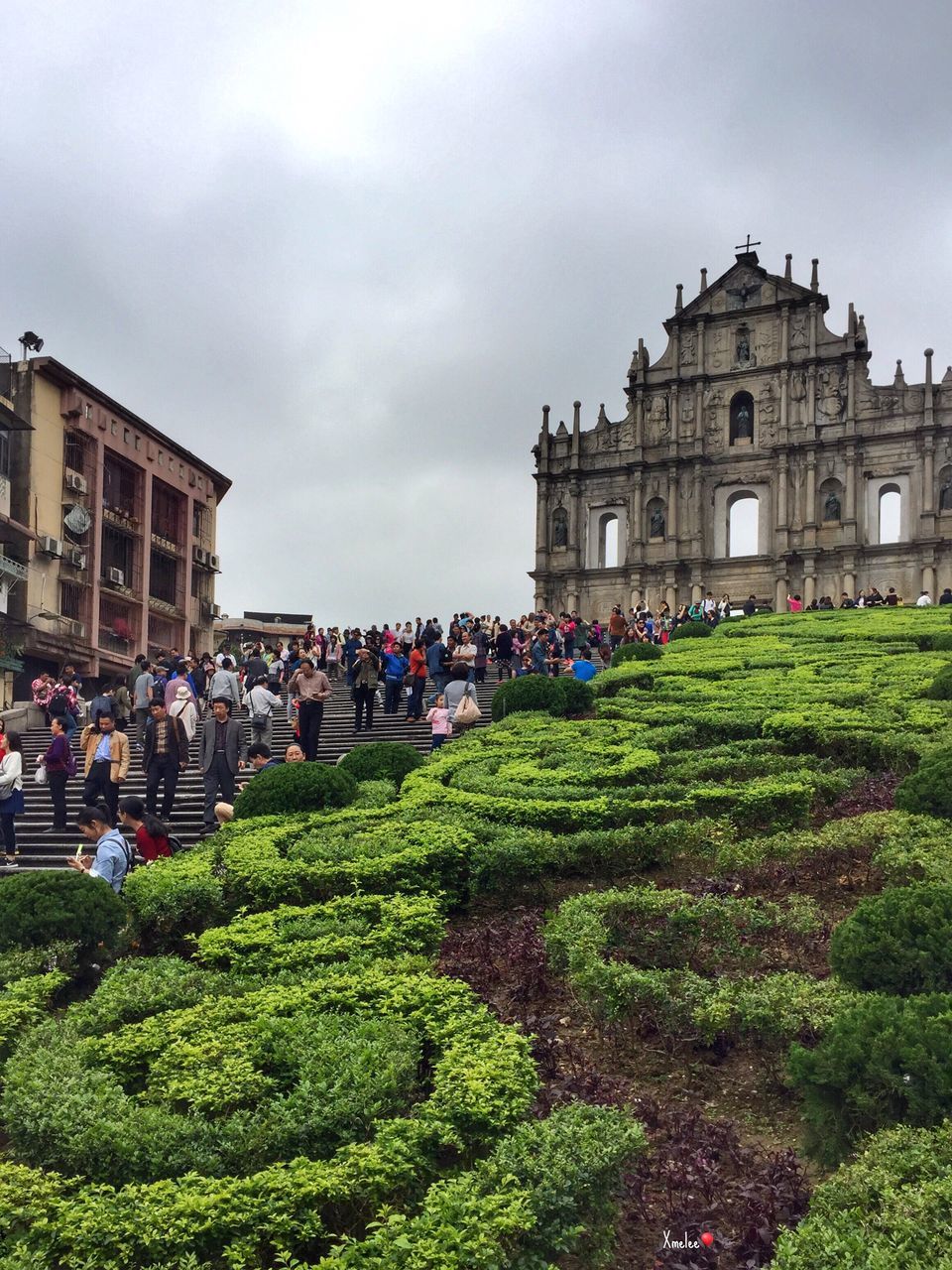 architecture, building exterior, large group of people, travel destinations, built structure, sky, flower, formal garden, plant, real people, cloud - sky, women, city, outdoors, grass, ornamental garden, sculpture, crowd, nature, day, statue, people, cultures, adult