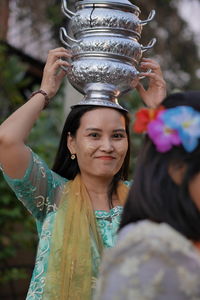 Portrait of smiling woman with face paint carrying stack containers on head during event