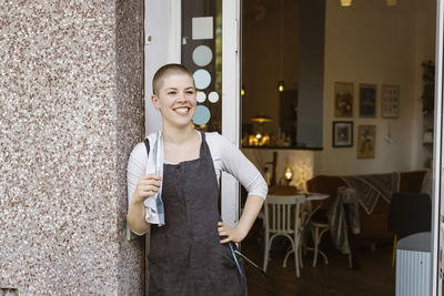 Happy female cafe owner with hand on hip standing near doorway