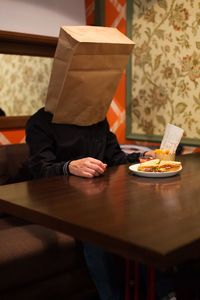 Man with paper bag on face while having sandwich in restaurant