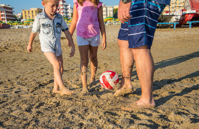 Father playing soccer with son and daughter on sand at beach