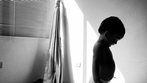 Side view of shirtless baby looking down while standing at home