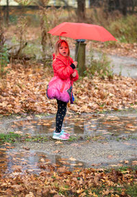 A cute little girl stands out in the rain with an umbrella, waiting for her school bus