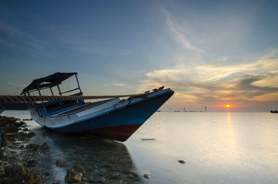 Boat moored on sea against sky during sunset