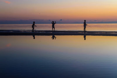 Silhouette people on beach against sky during sunset