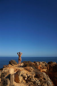 Woman standing on rock by sea against clear blue sky