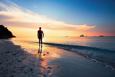 Rear view of silhouette man walking on beach at sunset